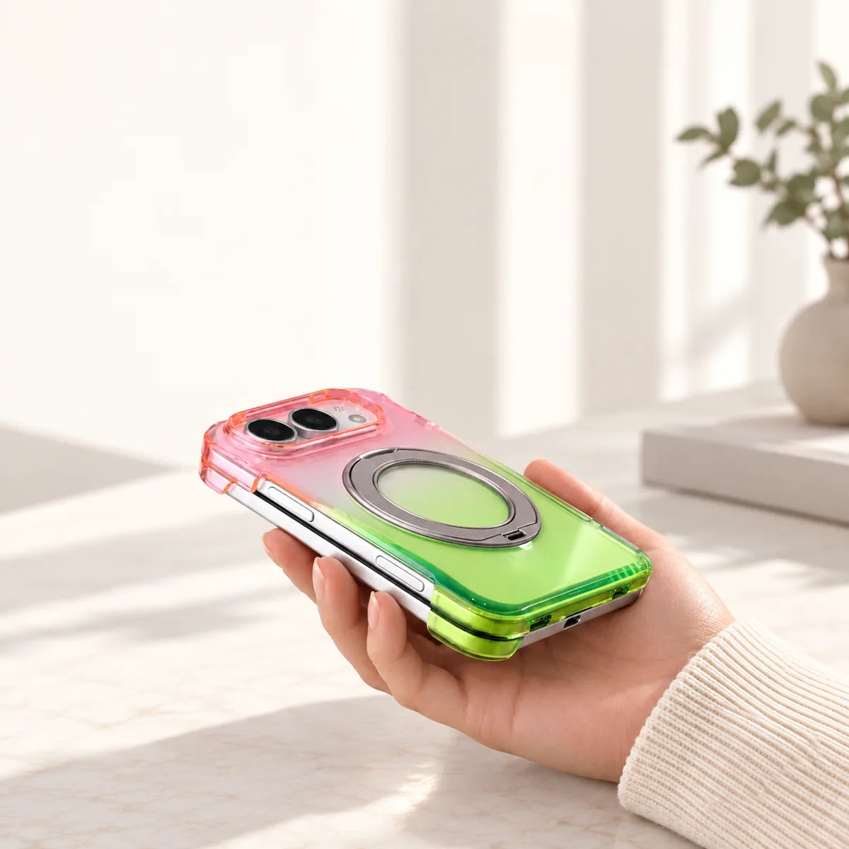 Shallow side view of a pink and green rear shell on a closed silver folding phone, held in a hand.